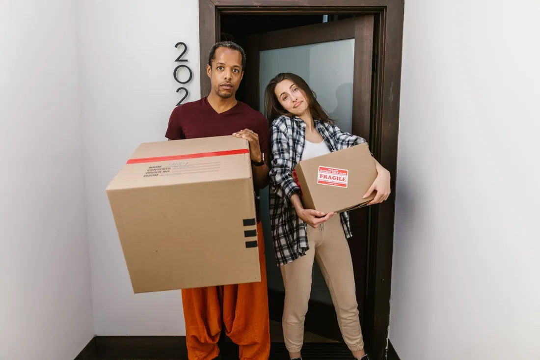 Zwei Personen tragen Umzugskartons durch eine Wohnungstür